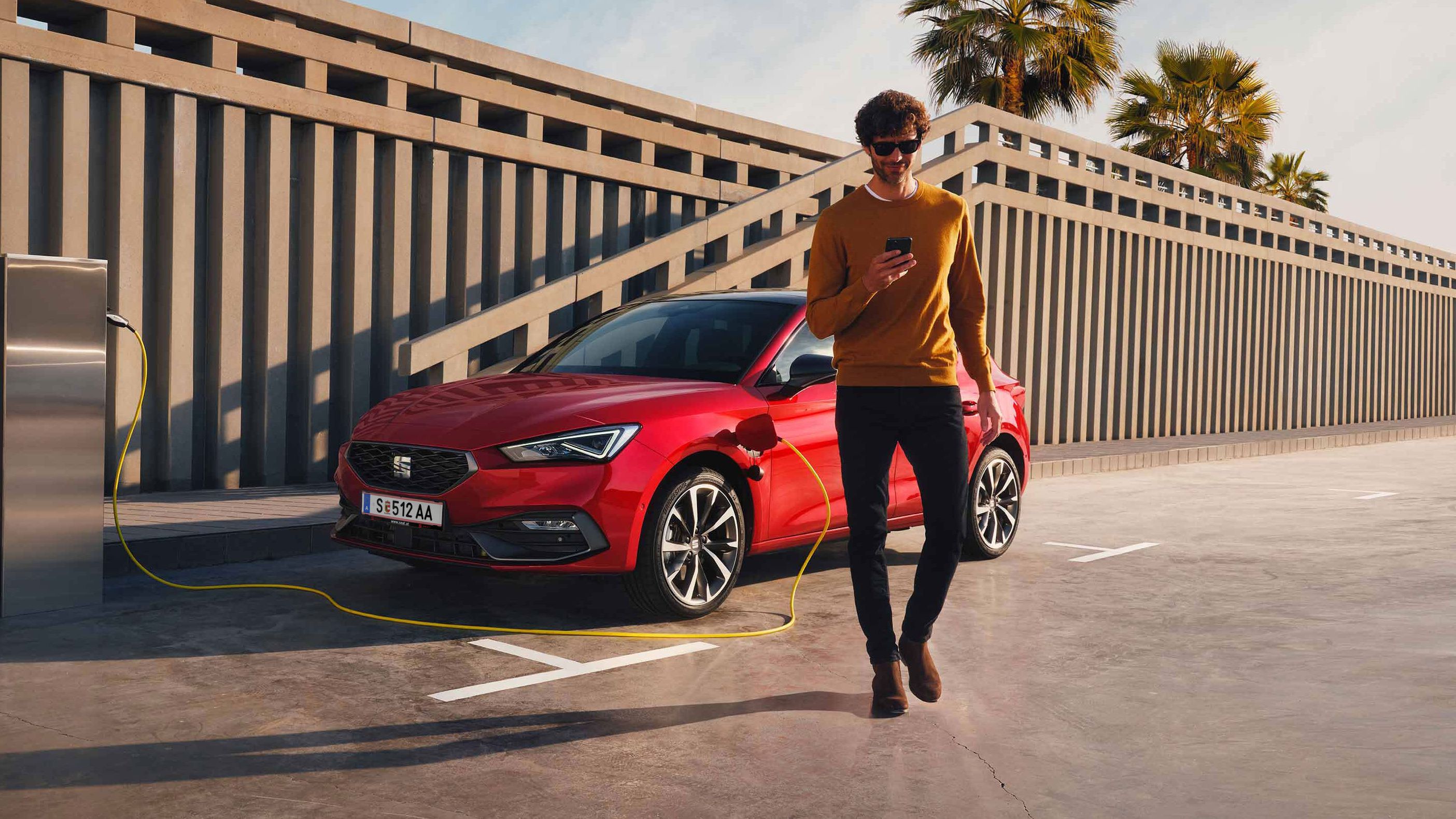 Ein Mann lädt seinen SEAT Leon Hybrid, checkt dabei die SEAT Connect App und geht dann vom Auto weg